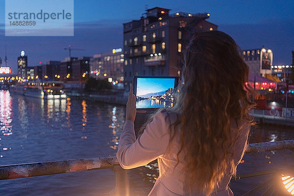 Junge Frau fotografiert mit einem digitalen Tablett auf einer Brücke  einem Fluss und einer Stadt im Hintergrund  Berlin  Deutschland