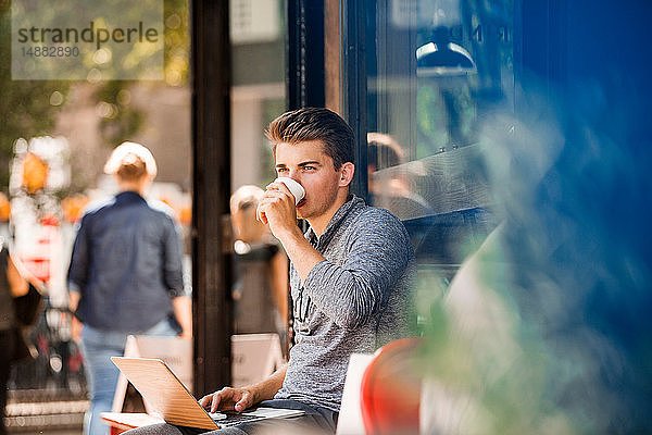 Junger Mann trinkt Kaffee und benutzt Laptop im Café