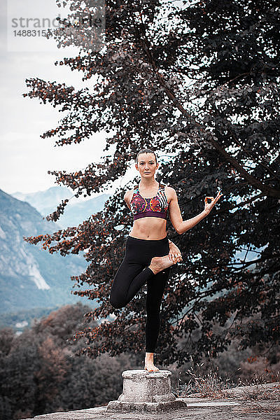 Frau praktiziert Yoga  balanciert auf einem Bein auf einem Sockel  Berglandschaft  Domodossola  Piemont  Italien