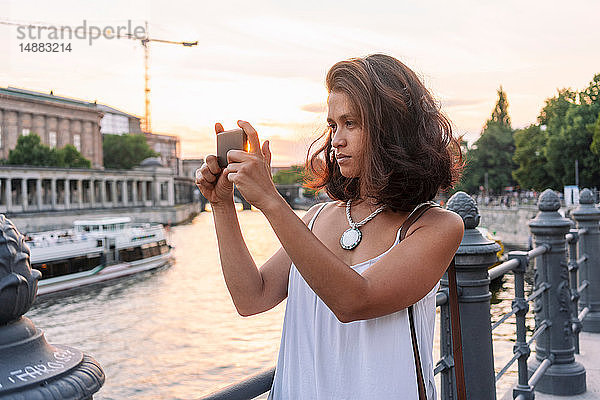 Studentin beim Fotografieren mit Smartphone am Fluss  Berlin  Deutschland