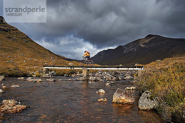 Männlicher Mountainbiker radelt über Steg in Bergtal-Landschaft  Achnasheen  Schottische Highlands  Schottland