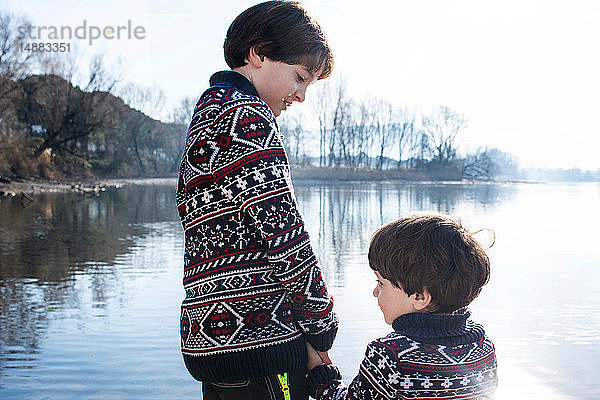 Junge und kleiner Bruder im passenden Pullover halten Händchen am Seeufer  Comer See  Lecco  Lombardei  Italien