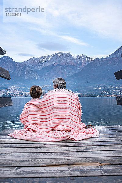 Junge und Vater in eine Decke gewickelt auf dem Seepier  Rückansicht  Comer See  Onno  Lombardei  Italien