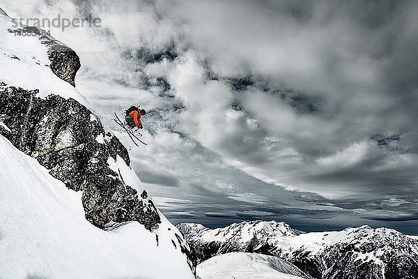 Männlicher Skifahrer springt in der Luft von einem schroffen Berghang  Alpe-d'Huez  Rhône-Alpes  Frankreich