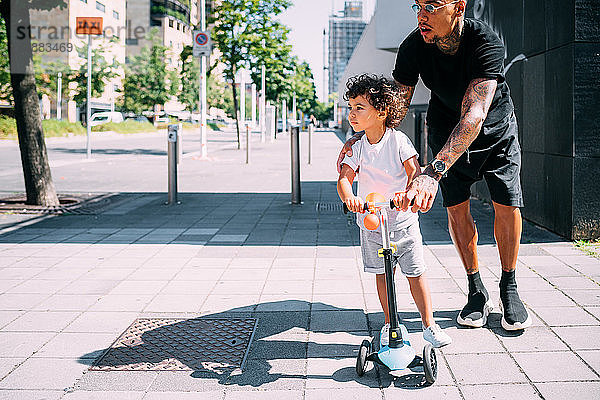Vater lehrt Sohn Schiebemotorroller auf Bürgersteig fahren