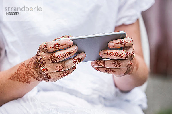 Frau mit Henna-Tattoo auf den Händen per Smartphone