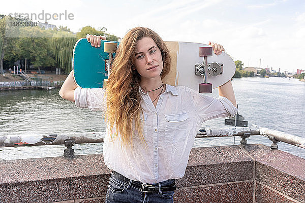 Junge Frau mit Skateboard auf der Schulter  Fluss im Hintergrund  Berlin  Deutschland