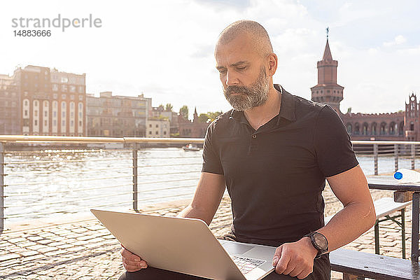 Mann mit Laptop auf Brücke  Fluss  Oberbaumbrücke und Gebäuden im Hintergrund  Berlin  Deutschland