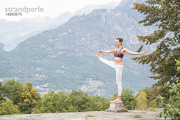 Frau praktiziert Yoga  balanciert auf einem Bein auf einem Sockel  Berglandschaft  Domodossola  Piemont  Italien