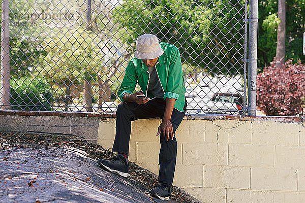 Junger Mann betrachtet Smartphone am Parkzaun  Los Angeles  Kalifornien  USA
