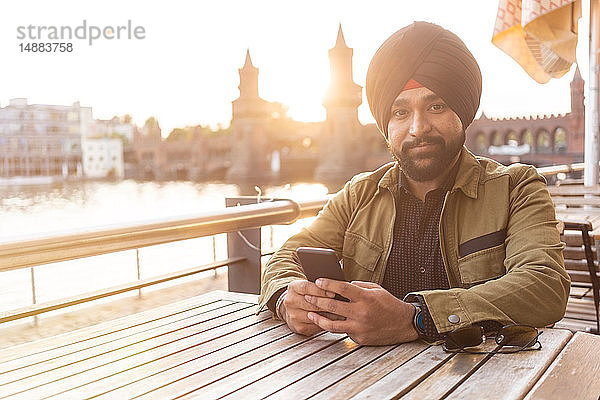 Indischer Mann benutzt Smartphone in Café am Fluss  Berlin  Deutschland