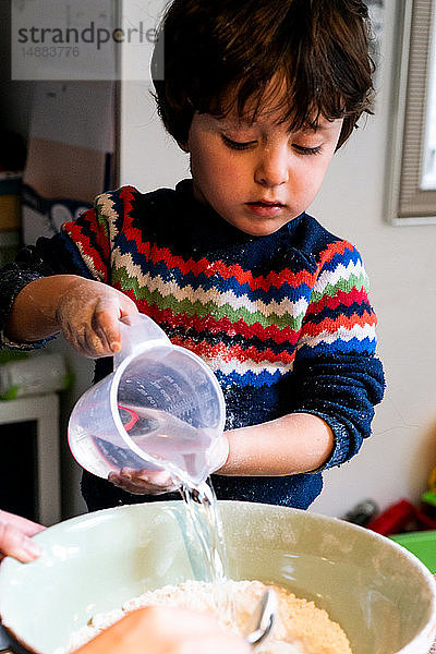 Kleinkind gießt Wasser in Mehl in Rührschüssel