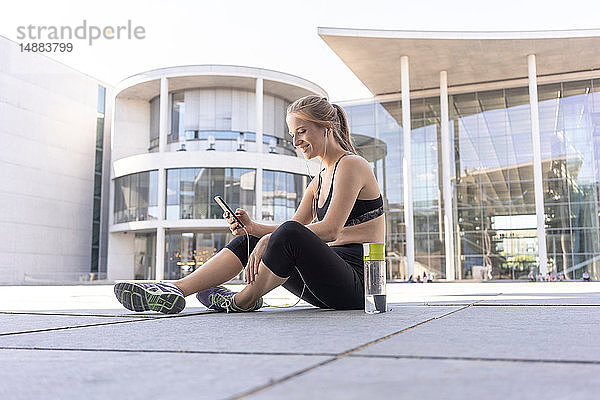 Junge Frau macht Pause vom Sport und benutzt Smartphone in der Stadt  Berlin  Deutschland