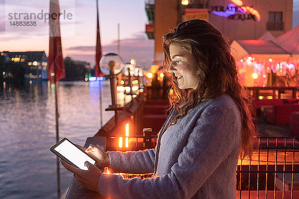 Junge Frau mit digitalem Tablett auf Brücke  Fluss und Stadt im Hintergrund  Berlin  Deutschland