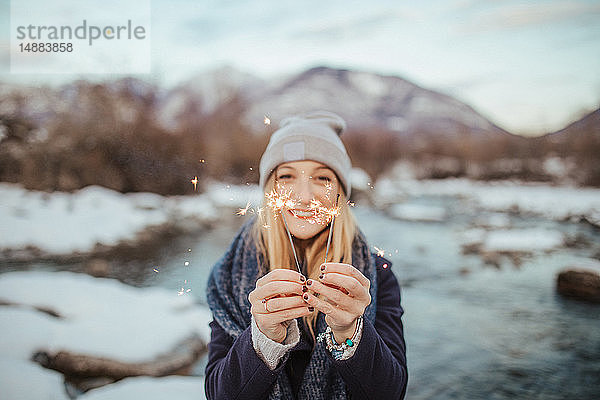 Frau mit Strickmütze mit Wunderkerzen in der Hand am schneebedeckten Flussufer  Porträt  Orta  Piemont  Italien