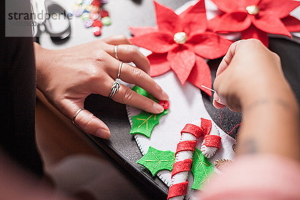 Über-Schulter-Ansicht einer Frau  die Stechpalmenbeeren auf Weihnachtsschmuck aufnäht  Detail der Hände