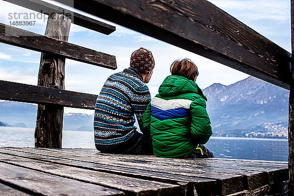 Junge und Vater sitzen am Pier am Seeufer  Rückansicht  Comer See  Onno  Lombardei  Italien