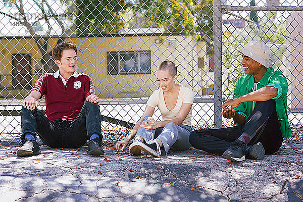 Drei junge erwachsene Freunde sitzen am Parkzaun  Los Angeles  Kalifornien  USA