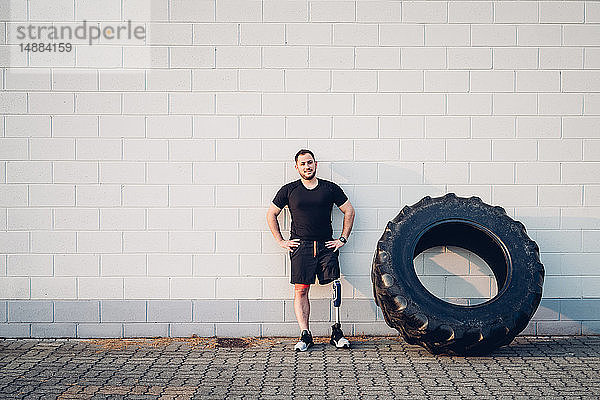 Mann mit Beinprothese lehnt an Wand neben Trainingsreifen