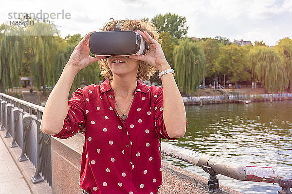 Junge Frau mit VR-Headset auf der Brücke  Fluss im Hintergrund  Berlin  Deutschland