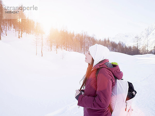 Junge Frau mit Strickmütze mit Blick auf die schneebedeckte Landschaft  Alpe Ciamporino  Piemont  Italien