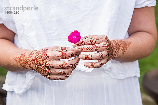 Frau in weißem Kleid mit Henna-Tattoo auf Händen  die eine Blume halten