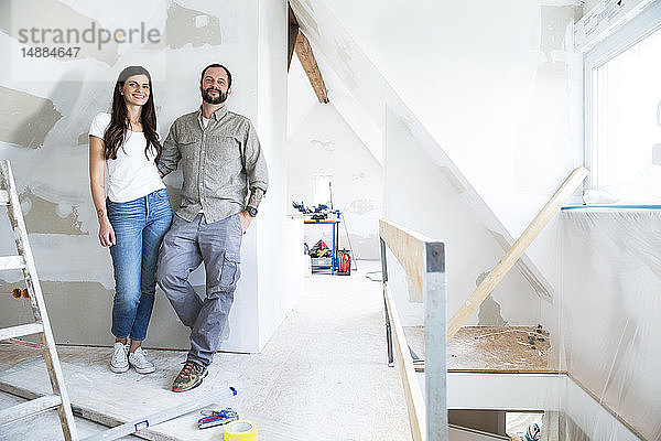 Porträt eines selbstbewussten Paares  das auf dem zu renovierenden Dachboden steht