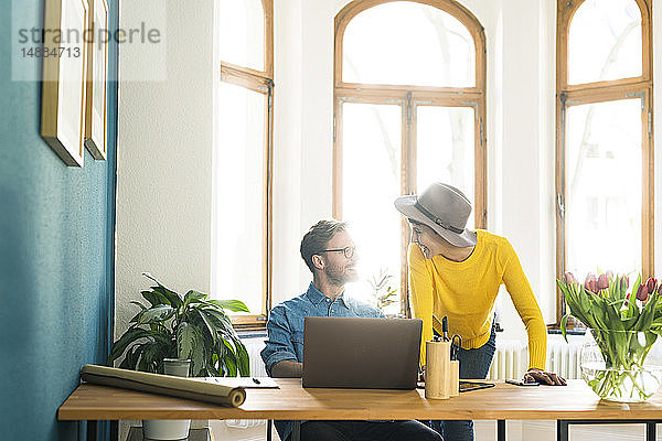 Gelegenheitsunternehmerpaar im Heimbüro  das am Laptop arbeitet und sich gegenseitig anlächelt