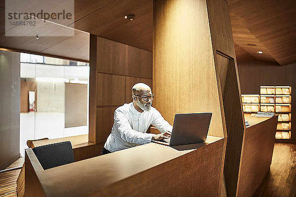 Älterer Mann arbeitet am Laptop am Arbeitsplatz in der Bibliothek