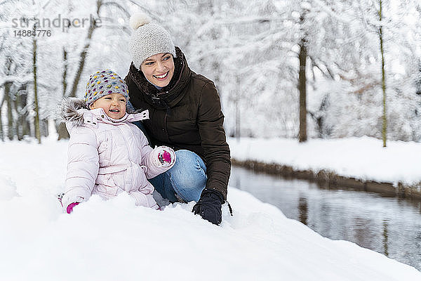 Glückliche Mutter mit Tochter an einem Wassergraben in Winterlandschaft