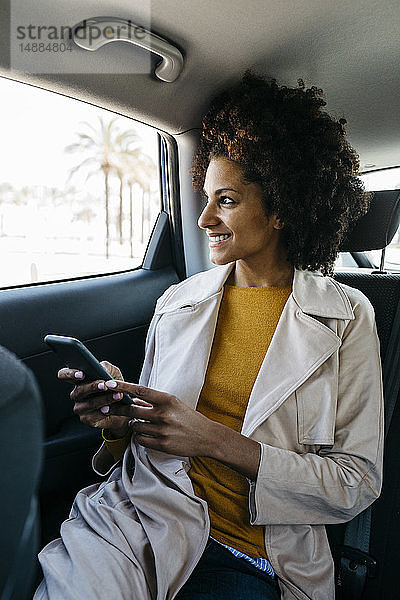 Lächelnde Frau sitzt auf dem Rücksitz eines Autos und hält ein Handy