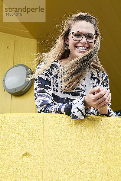 Porträt einer lachenden blonden Frau mit wehendem Haar  die sich an eine gelbe Balustrade lehnt