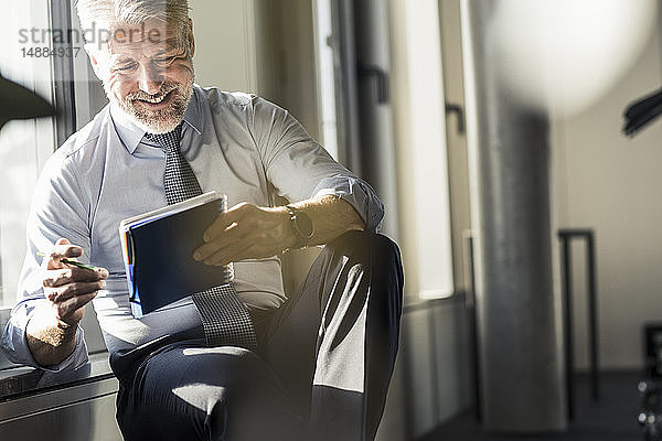 Lächelnder reifer Geschäftsmann am Fenster sitzend mit Notebook