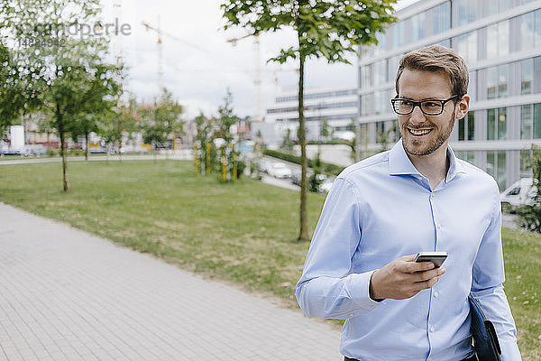 Junger Geschäftsmann geht im Park spazieren  benutzt Smartphone