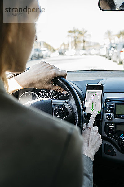 Frau fährt mit einem Auto durch die Stadt und nutzt eine Telefon-Navigationsanwendung