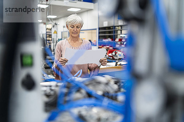 Ältere Frau betrachtet Plan in einer Fabrik