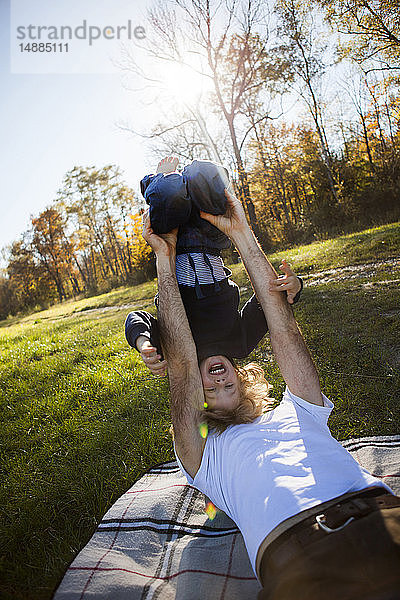 Lachender kleiner Junge beim Kopfstand mit Hilfe seines Vaters im Freien