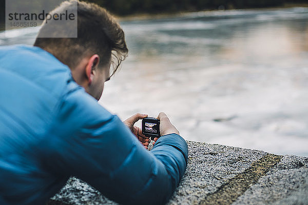 Junger Mann fotografiert einen zugefrorenen See mit einer kleinen Kamera
