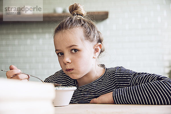 Skeptisches Mädchen sitzt in der Küche und isst Müsli