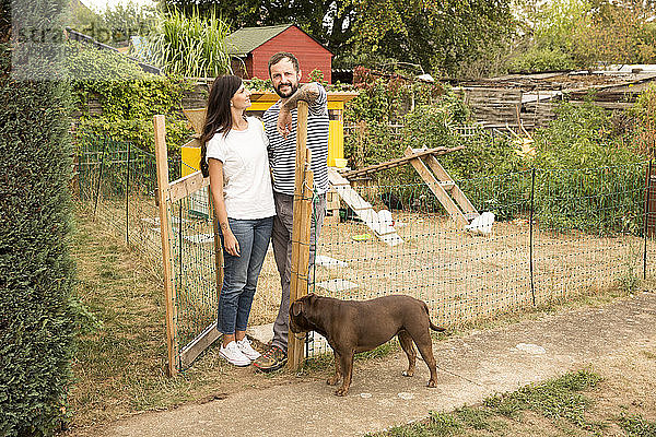 Porträt eines Ehepaares mit Hund beim Hühnerstall im Garten stehend