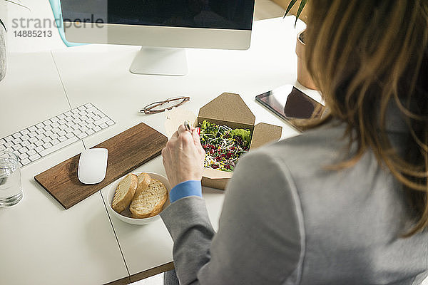Frau isst Salat zum Mittagessen an ihrem Schreibtisch