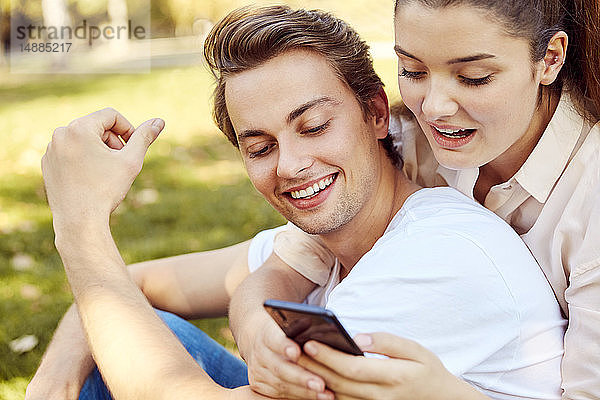 Junges Paar betrachtet Smartphone in einem Park
