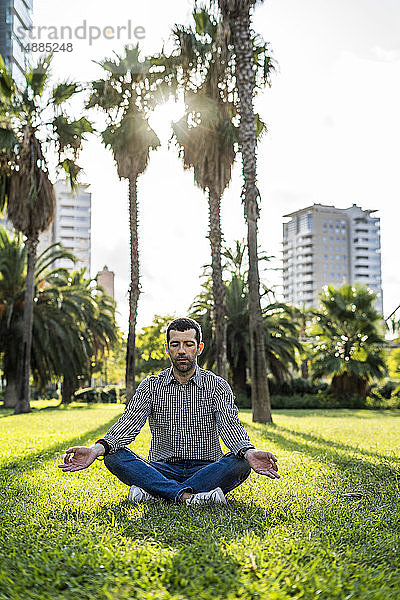 Mann sitzt auf einer Wiese im Stadtpark und macht Yoga-Übungen