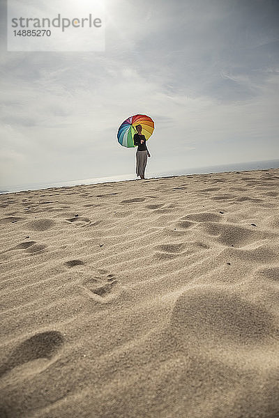 Frau mit buntem Regenschirm am Strand stehend