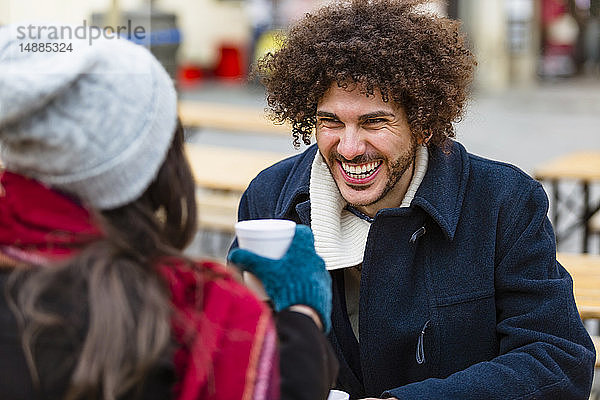 Glückliches junges Paar mit heißen Getränken auf dem Weihnachtsmarkt