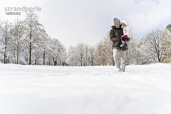 Vater trägt Tochter  die in Winterlandschaft spazieren geht