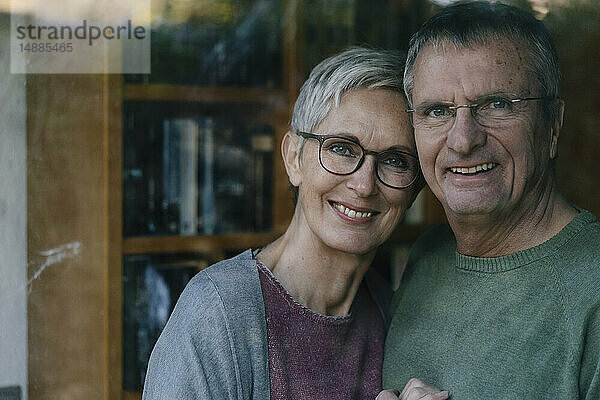 Porträt eines glücklichen älteren Paares hinter einer Fensterscheibe