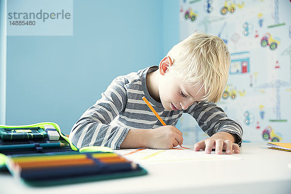 Fokussierter Junge macht Hausaufgaben am Schreibtisch im Kinderzimmer