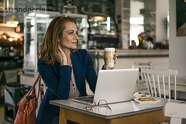 Geschäftsfrau sitzt im Café  isst zu Mittag  arbeitet am Laptop
