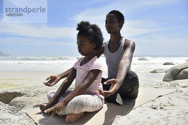 Mutter mit Tochter bei einer Yoga-Übung am Strand